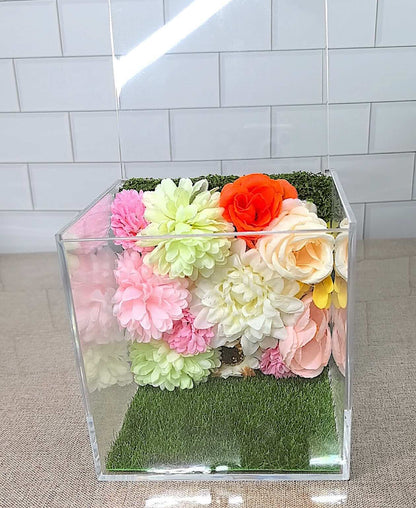 Interior view of a 3D pet memorial shadow box featuring a faux grass base and a bright artificial floral background.