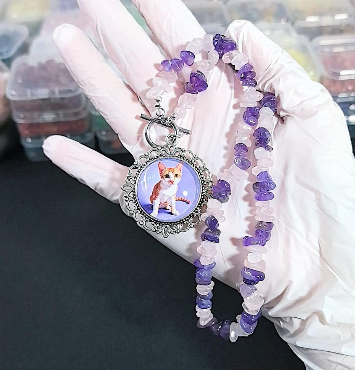 A gloved hand holding a customized pet memorial necklace featuring an everyday snapshot of a cat inside a vintage-style alloy pendant with a front toggle clasp.