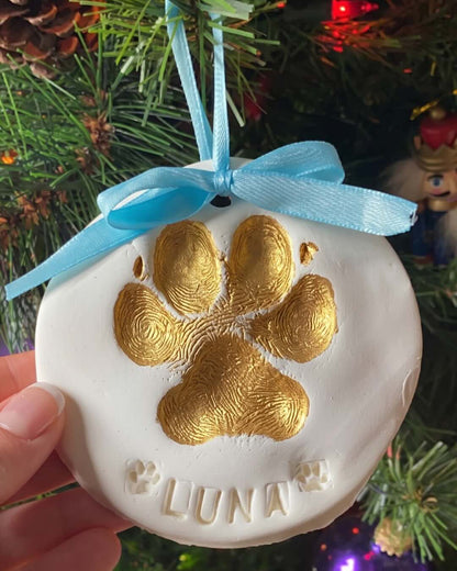 Round dog paw print ornament with the name Luna hanging on a Christmas tree