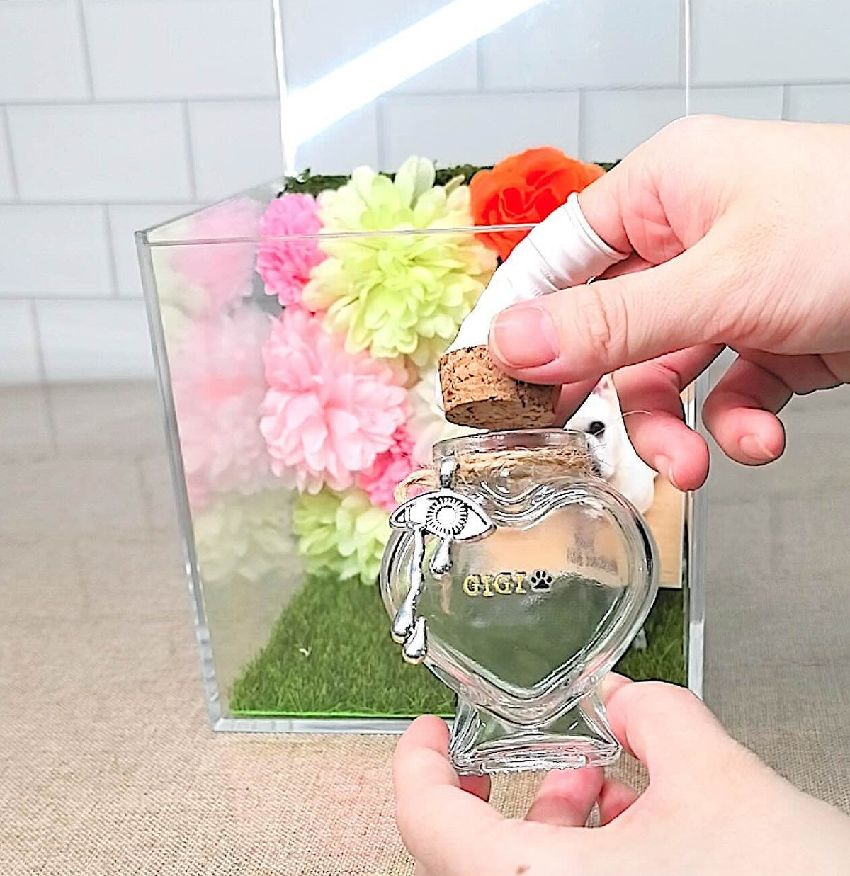 Hands holding a personalized heart-shaped glass pet fur keepsake bottle with a cork stopper.
