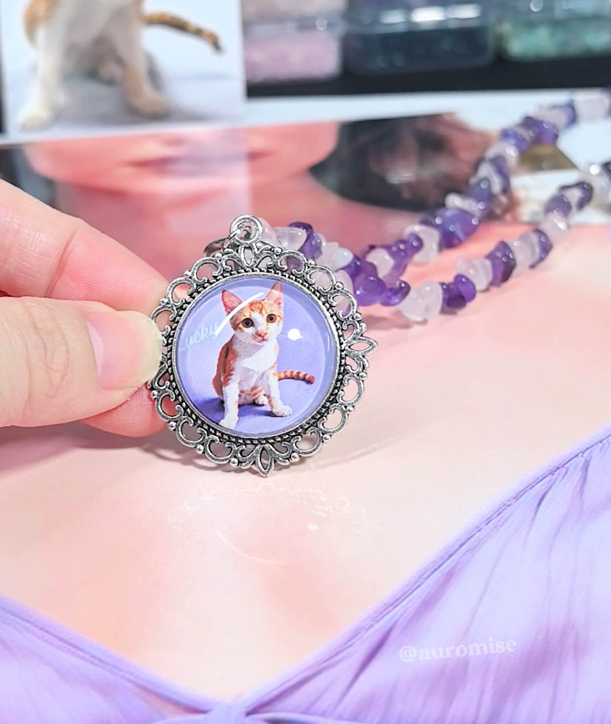 Close up of a hand holding a custom pet memorial pendant displaying a printed cat photo in a silver frame.
