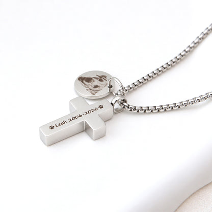 Close-up of a silver stainless steel pet memorial cross necklace engraved with a dog's name and dates, beside a round photo charm.